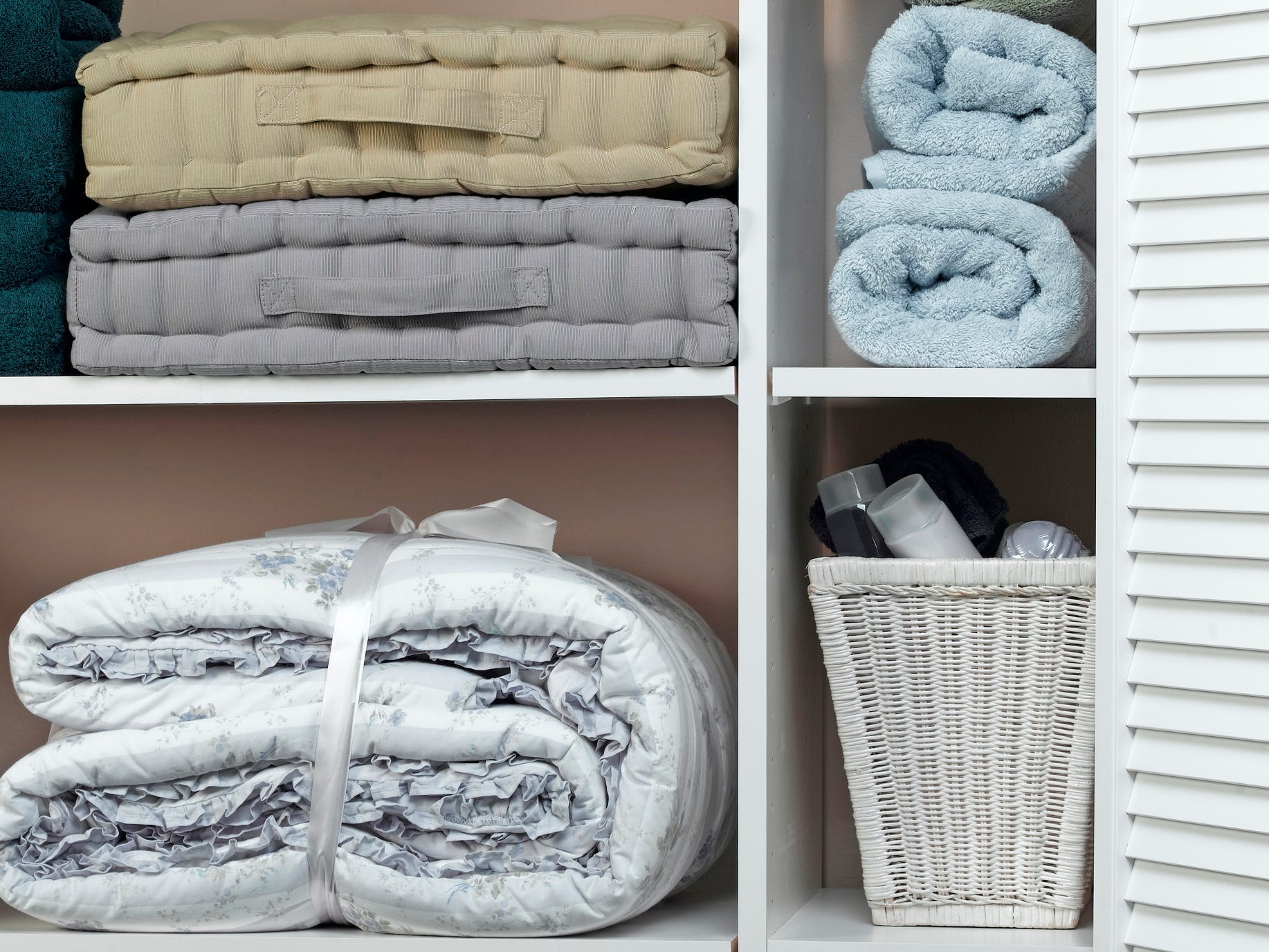 A closet with a comforter, bedding, a basket of items, and rolled towels.