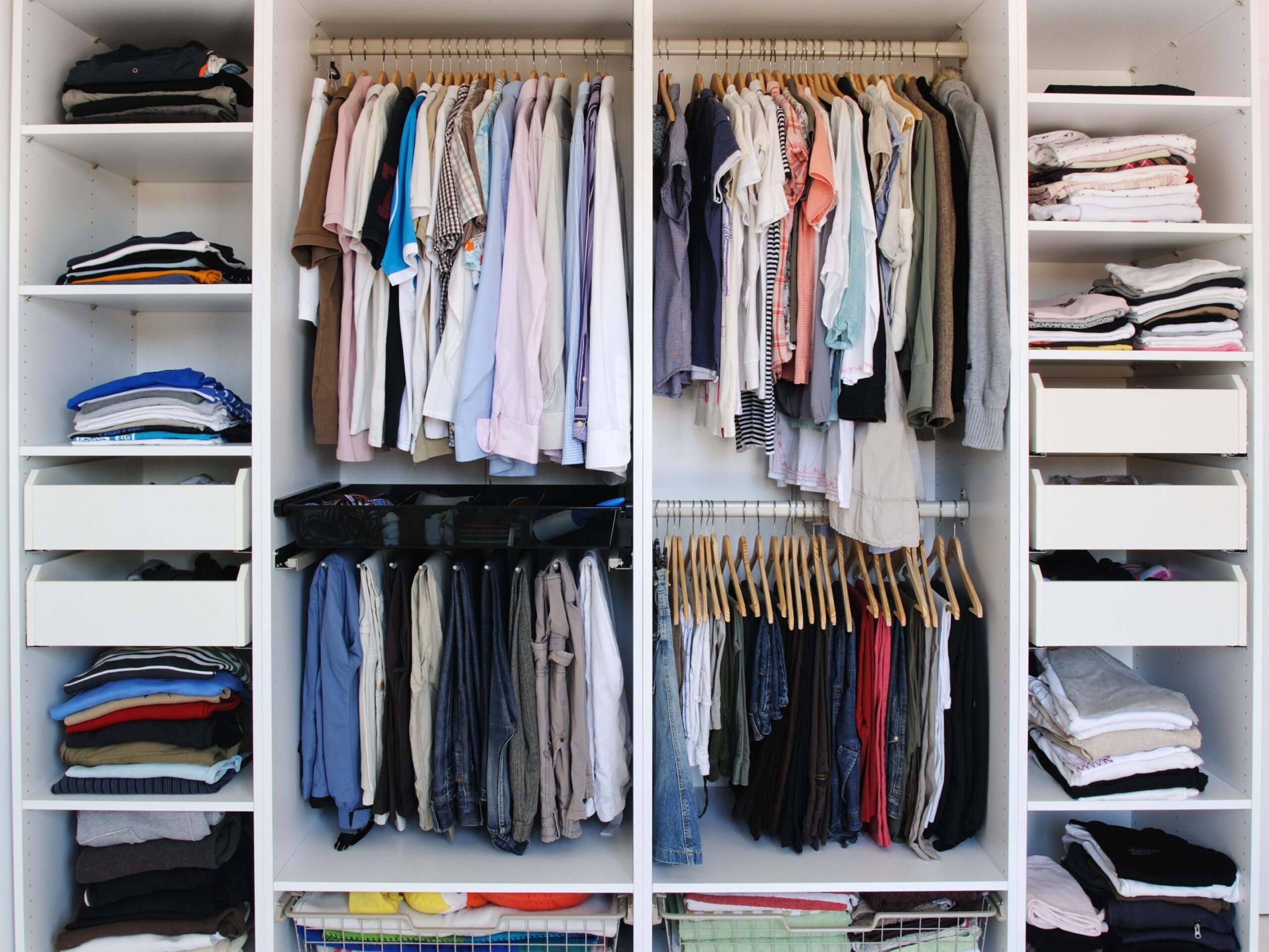 A closet full of men's clothing. Some items are hung, some are folded on shelves and in baskets, and some are in drawers.