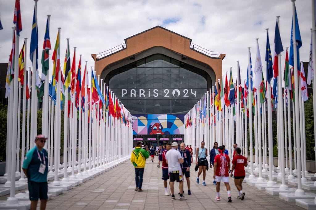 De ingang van de etenszaal in het Olympisch dorp met twee rijen vol vlaggen aan beide kanten.