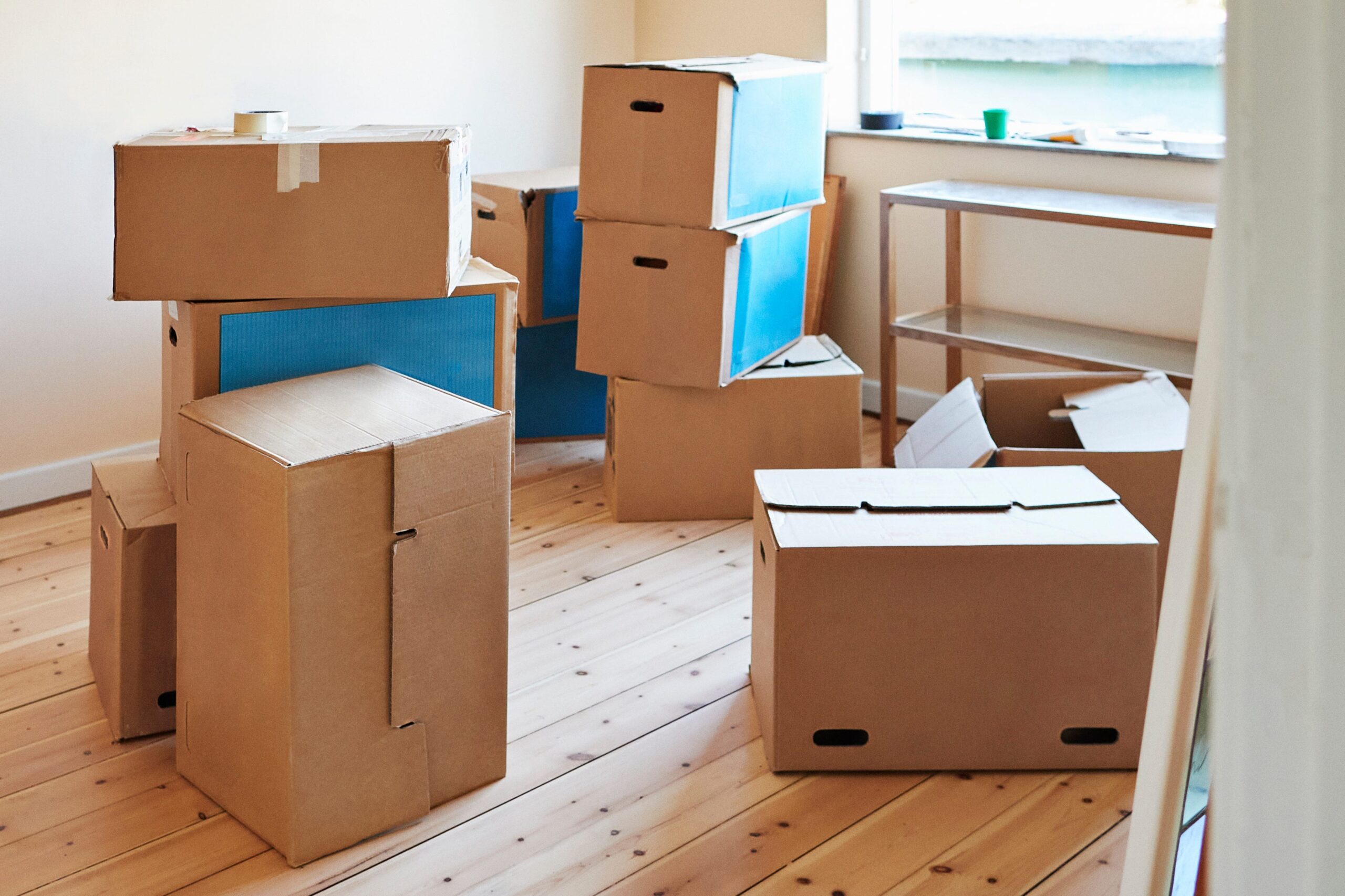 Cardboard boxes stacked on top of each other in a room with a wooden floor and blank walls.