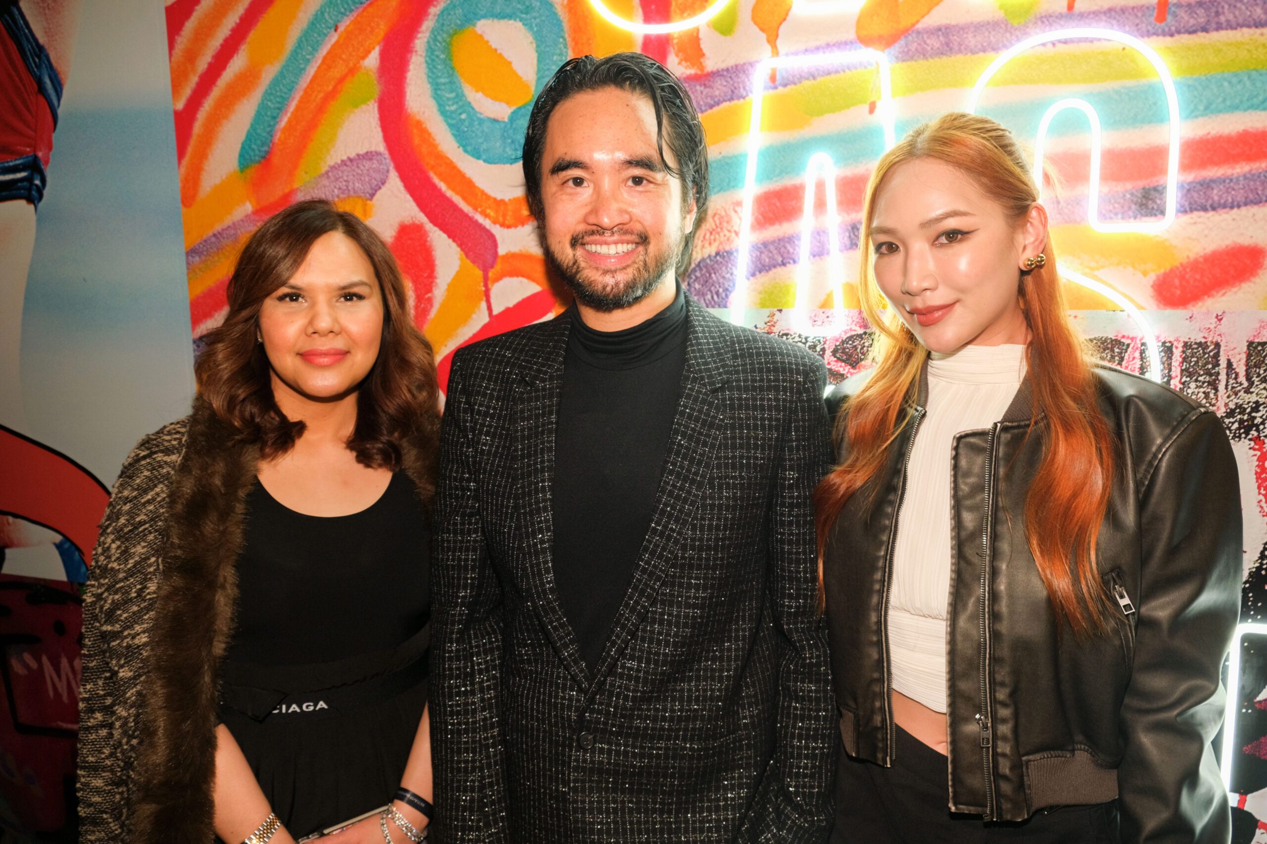 Adrian Cheng standing with two women in front of a graffiti-style mural.