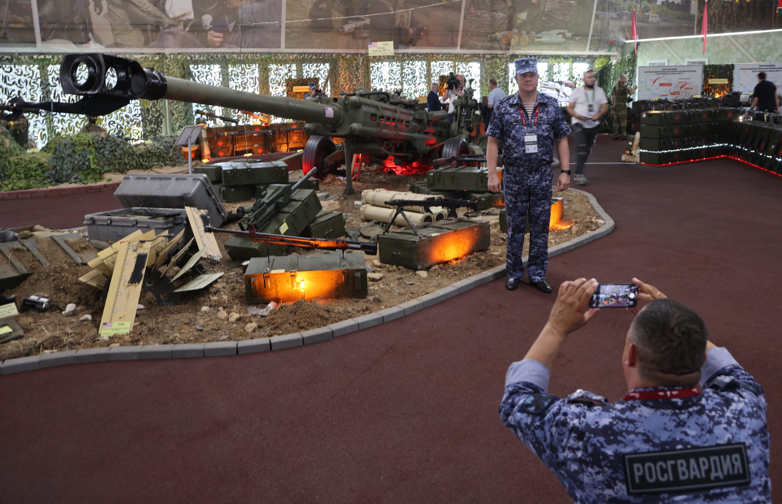 Een officier van de Russische Nationale Garde poseert voor een foto voor een display met buitgemaakte Oekraïense wapens.