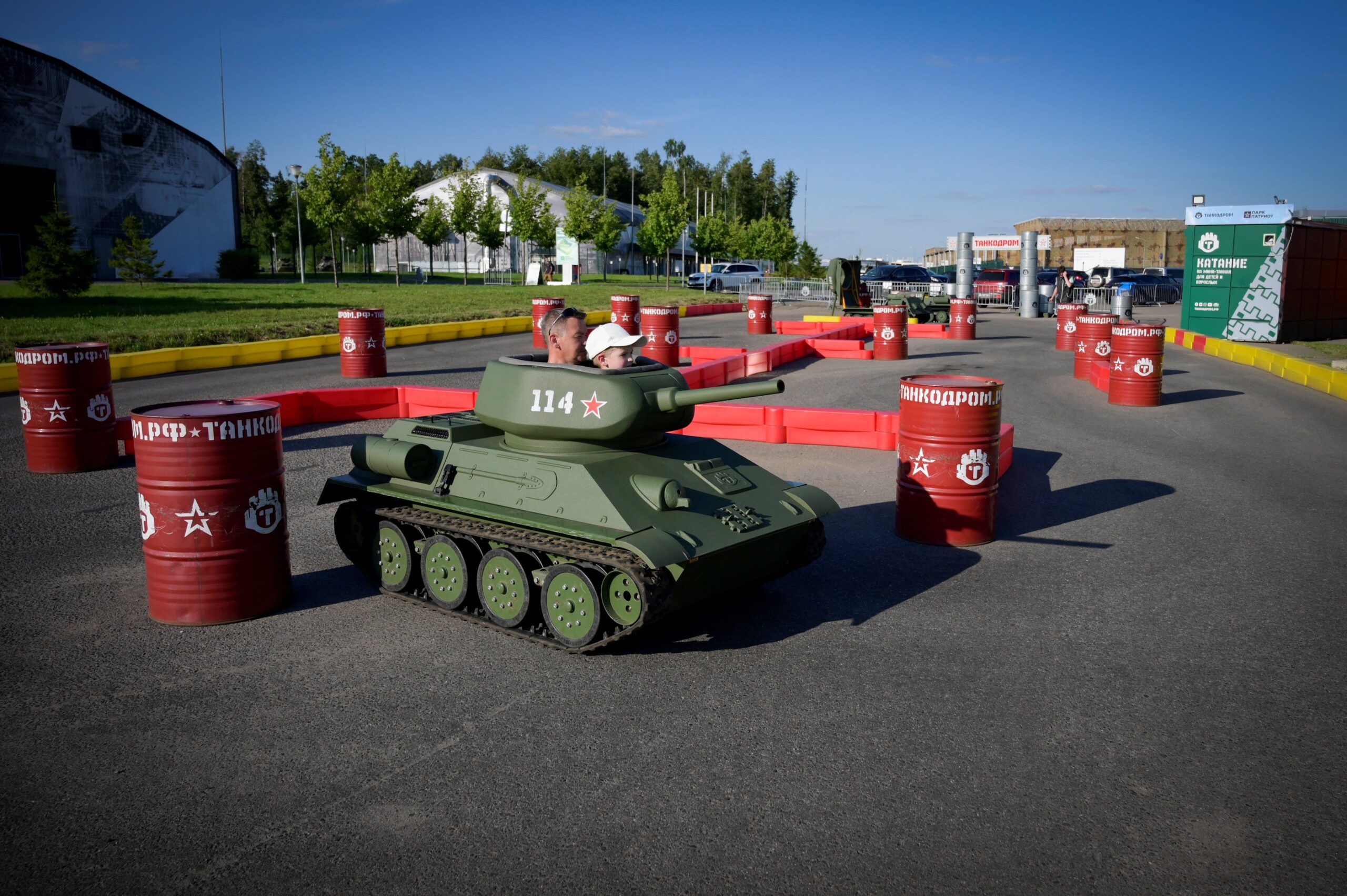 Een man en een jongen rijden in een speelgoedtank rond een parcours in Patriot Park.