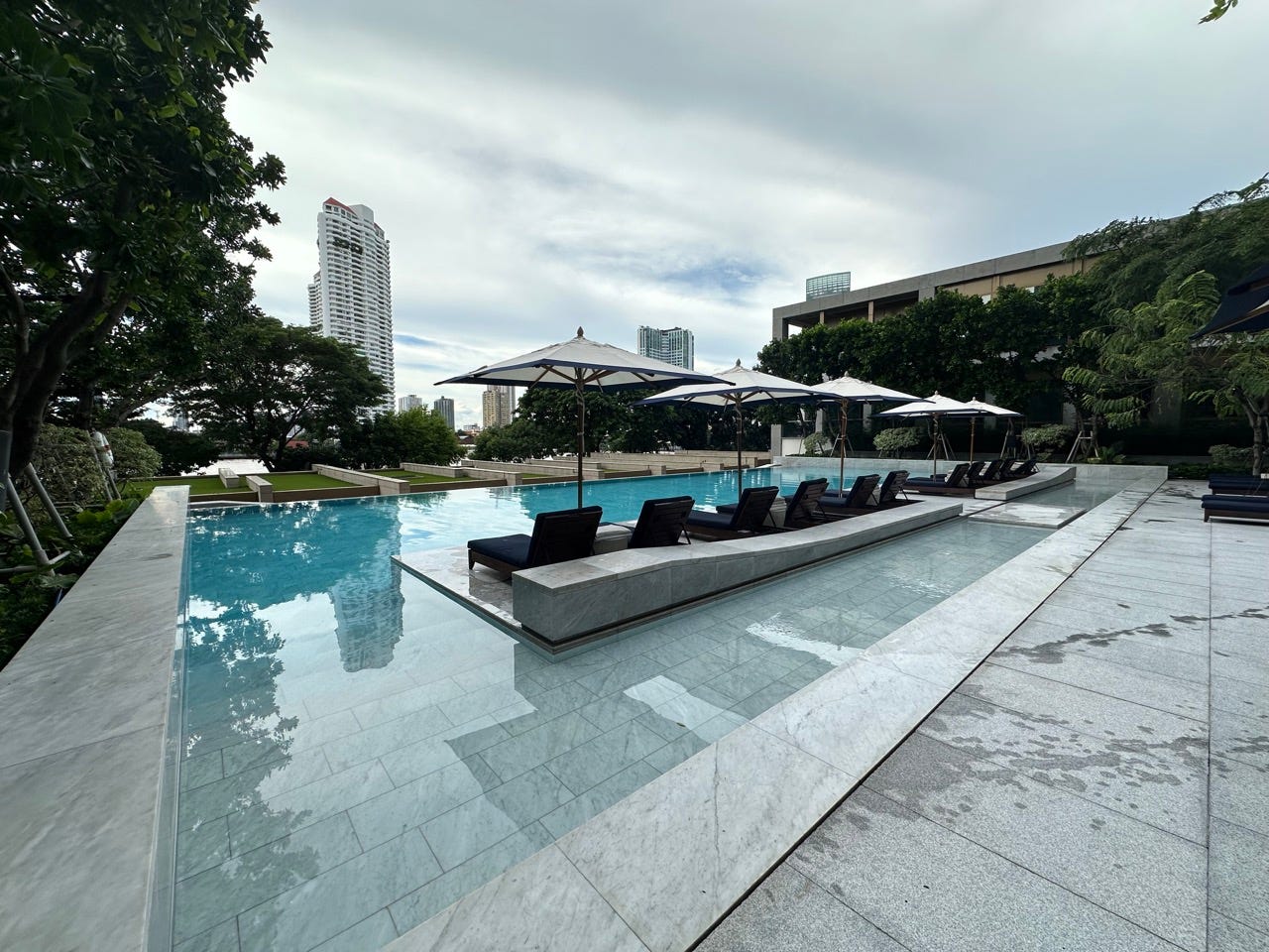 Large swimming pool with lounge chairs and umbrellas lined up around it 