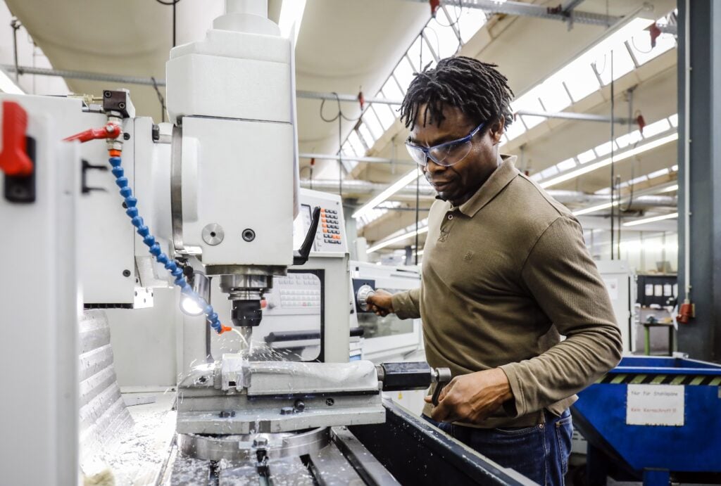 Een stagiair bewerkt metaal in een fabriek, in afwachting van zijn stagevergoeding.