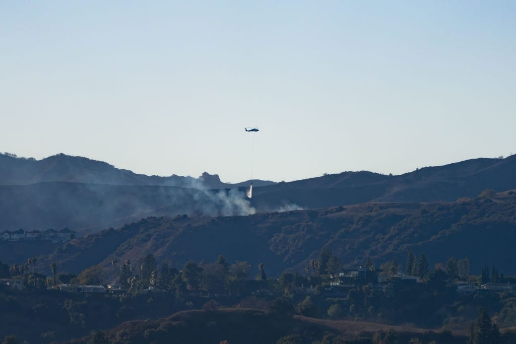 A firefighting helicopter drops water on the Hollywood Hills.