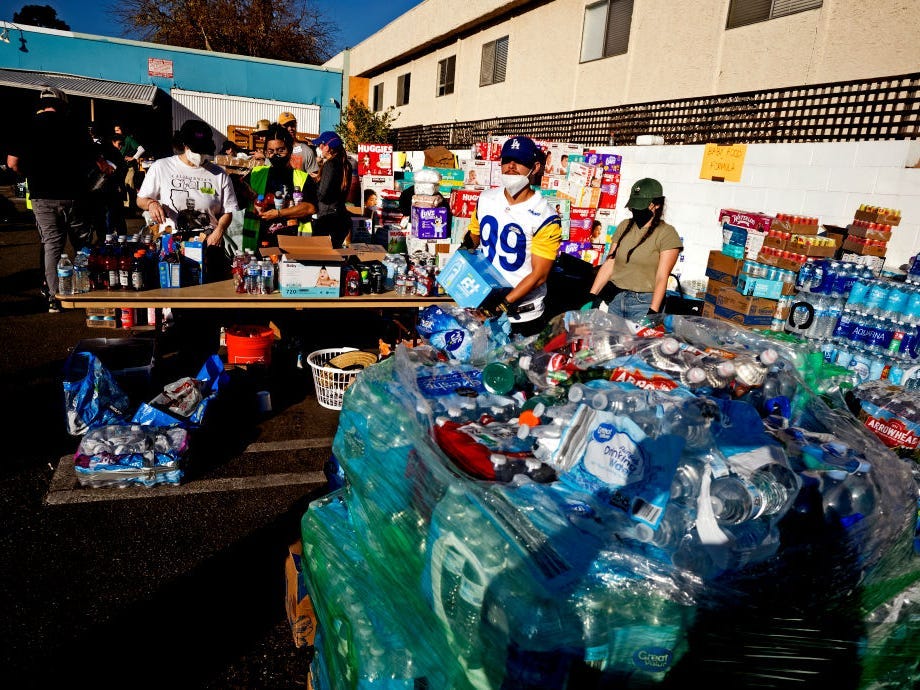 Volunteers help people load bags of goods at a large donation site that has sprung up at the Pasadena Community Job Center