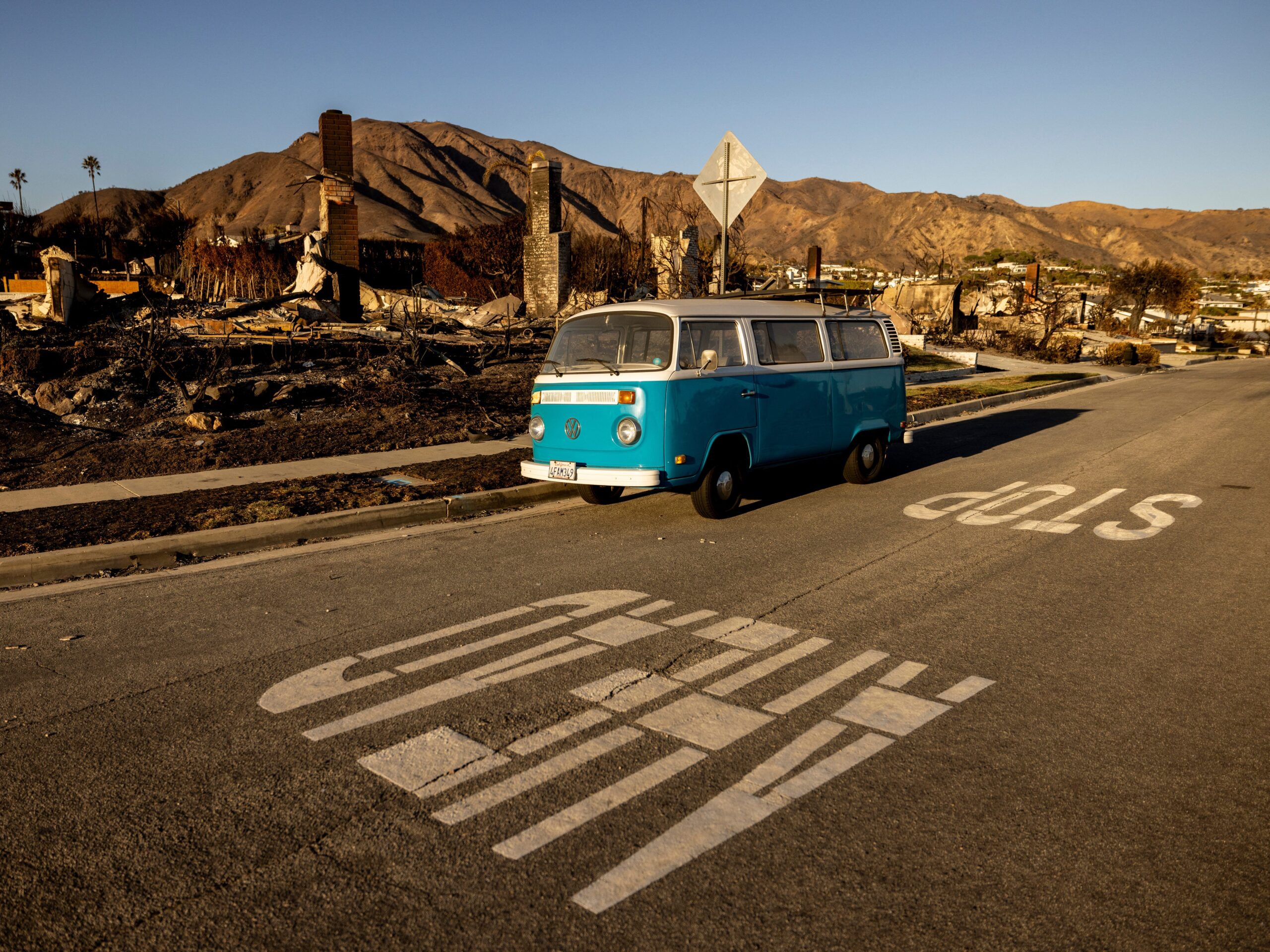 A blue Volkswagen van parked on the street in front of a block of homes destroyed in the Palisades Fire in Malibu.