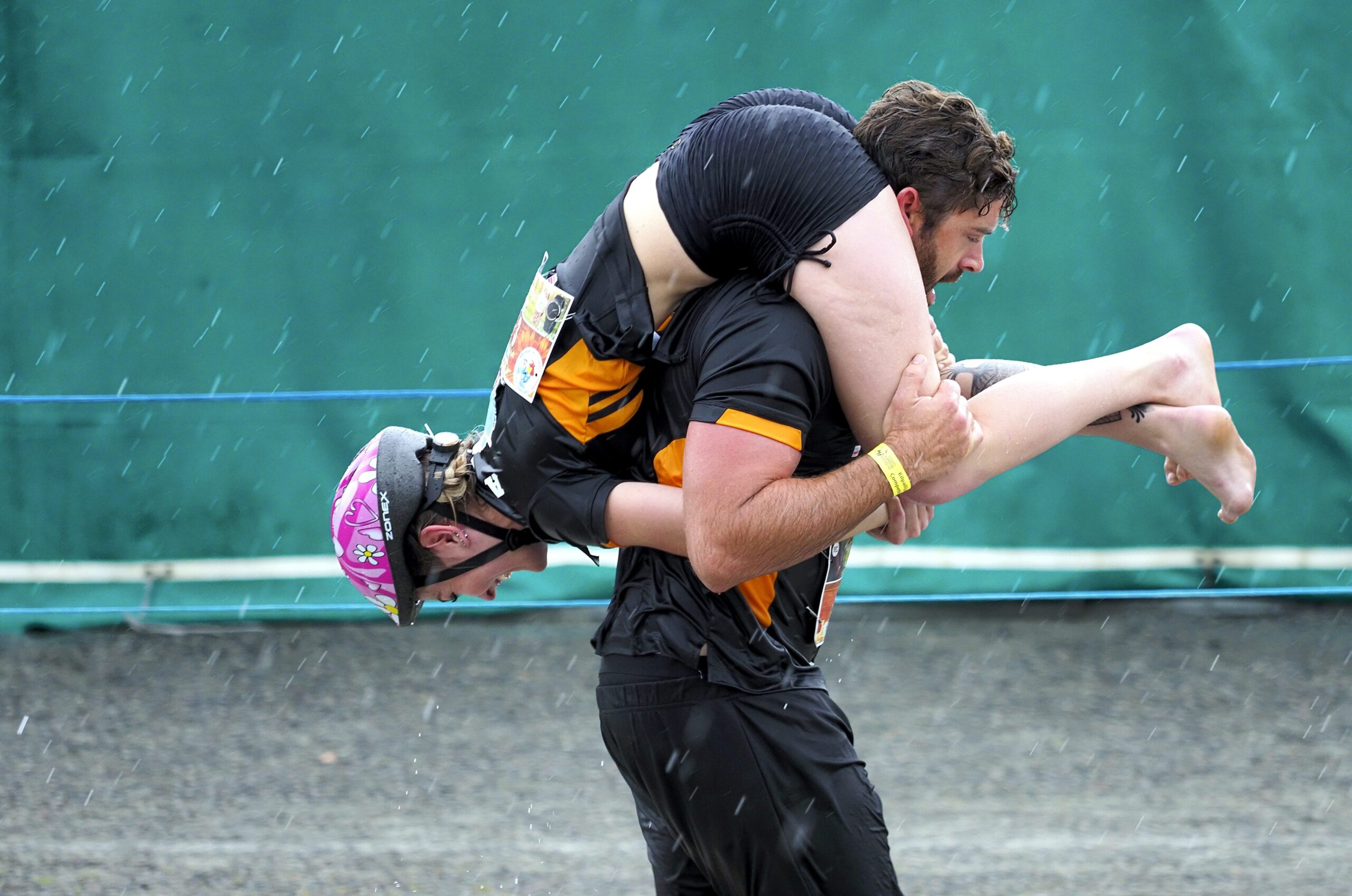 A man carries a woman backwards over his shoulders so her head faces his back