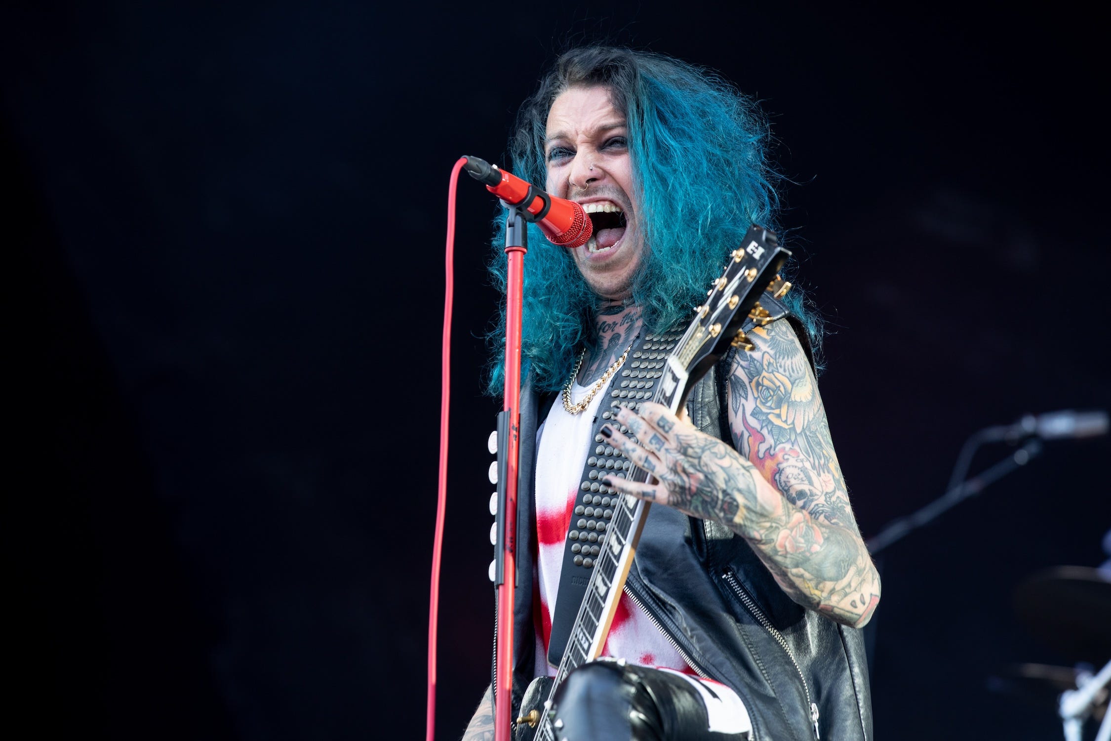 Samy Elbanna of  pLost Society, who has blue hair and full arm sleeve of tattoos, holds a guitar and sings into a red microphone