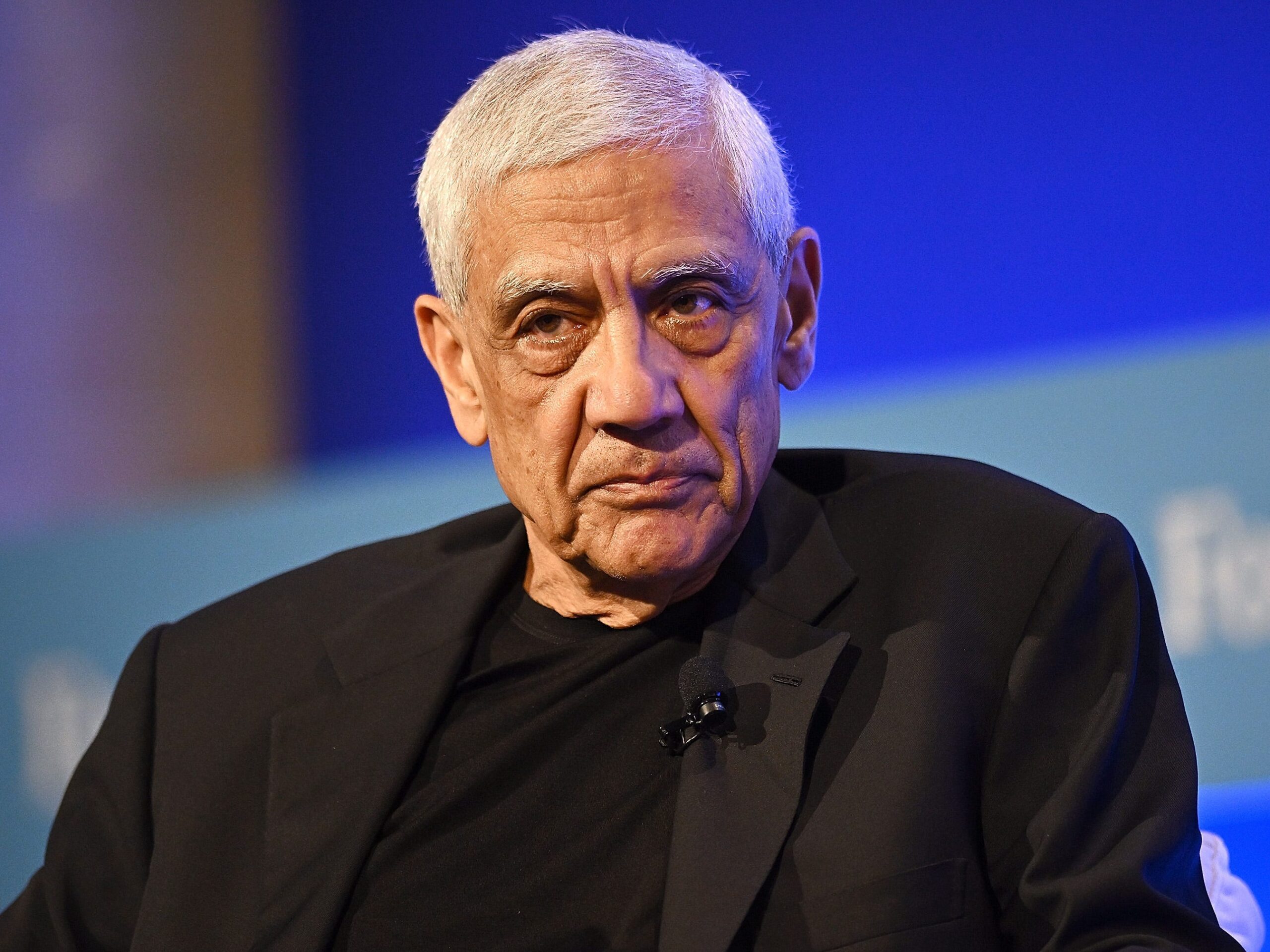 Vinod Khosla is pictured at an event, with a microphone clipped to his suit jacket.