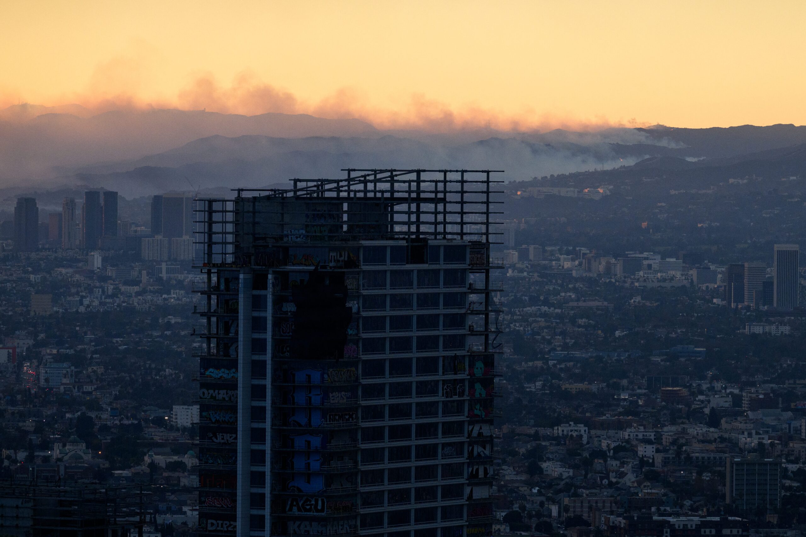 Smoke rises in an orange sky behind a tall, unfinished building