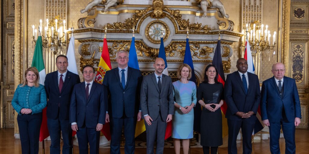 Een groep Europese en Oekraïense ministers poseert voor een foto tijdens de Weimar+ bijeenkomst in het Franse ministerie van Buitenlandse Zaken in Parijs op 12 februari 2025. De bijeenkomst richtte zich op de rol van Europese landen in de onderhandelingen over de toekomst van Oekraïne. Op de achtergrond zijn vlaggen van verschillende Europese landen te zien in een rijkelijk versierde zaal.