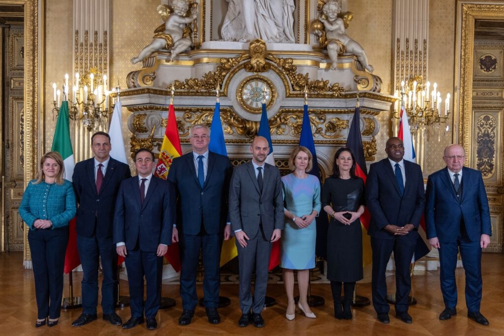 Een groep Europese en Oekraïense ministers poseert voor een foto tijdens de Weimar+ bijeenkomst in het Franse ministerie van Buitenlandse Zaken in Parijs op 12 februari 2025. De bijeenkomst richtte zich op de rol van Europese landen in de onderhandelingen over de toekomst van Oekraïne. Op de achtergrond zijn vlaggen van verschillende Europese landen te zien in een rijkelijk versierde zaal.