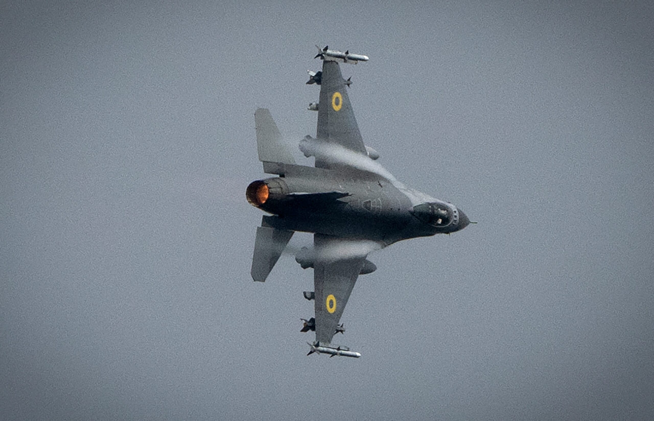 Een F-16 straaljager vliegt door de grijze lucht.