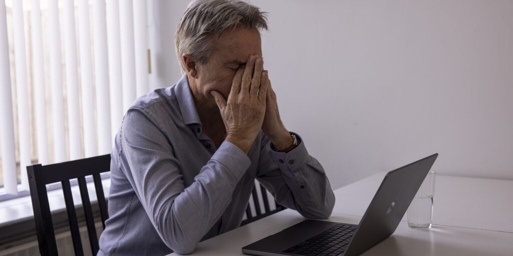 Een werkloos geraakte zzp'er kijkt getroffen naar een slecht bericht op zijn laptop. Hij zit aan zijn tafel in de huiskamer te werken.