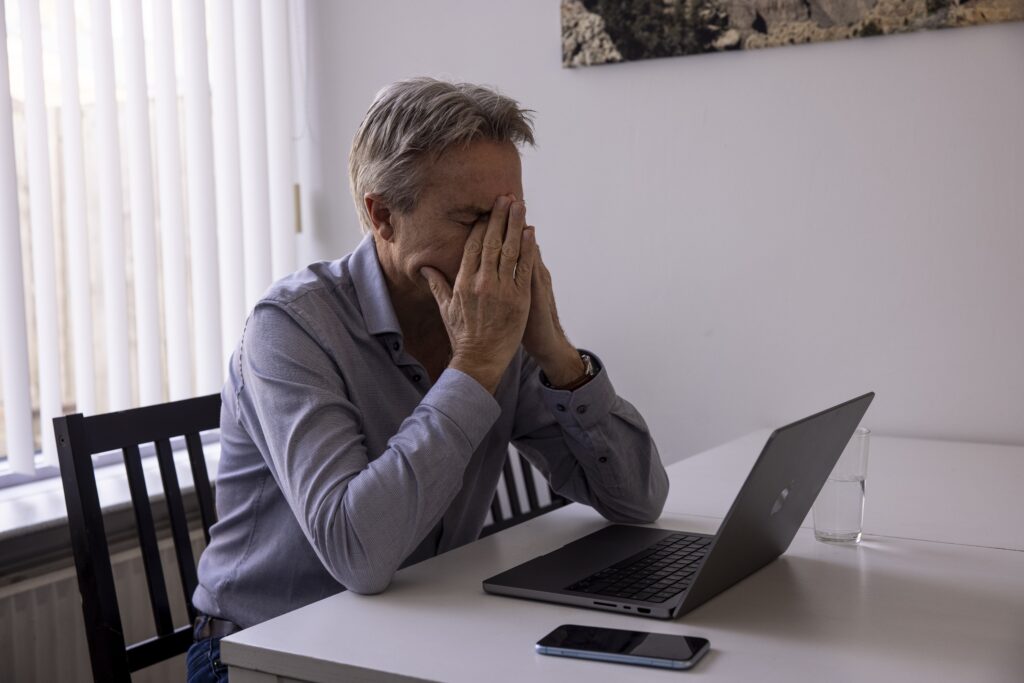 Een werkloos geraakte zzp'er kijkt getroffen naar een slecht bericht op zijn laptop. Hij zit aan zijn tafel in de huiskamer te werken.
