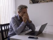 Een werkloos geraakte zzp'er kijkt getroffen naar een slecht bericht op zijn laptop. Hij zit aan zijn tafel in de huiskamer te werken.